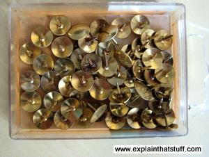 Gold thumbtack drawing pins in a plastic box.