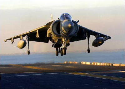 An AV-8B II Harrier lands on the flick deck of a ship.