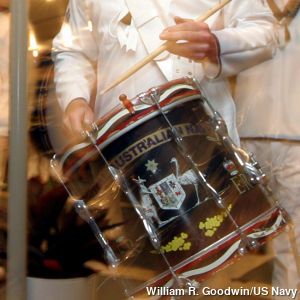 A marching navy drummer hits a drum with his sticks