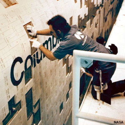 A man attaches refractory heat-protective white tiles to the surface of the Space Shuttle.