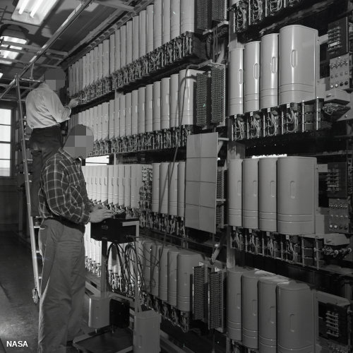 Telephone exchange in 1952 showing two men inspecting banks of relays via US National Archives catalog id 354793444.